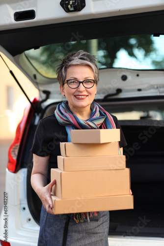 Smiling mature woman is loading cardboard boxes into the car.