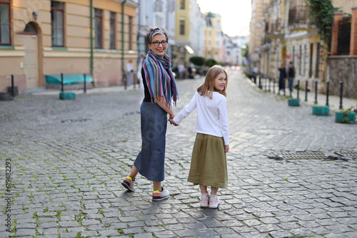 Grandmother and granddaughter walk through an old European city.