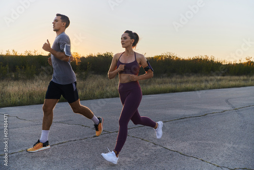 A handsome young couple running together during the early morning hours, with the mesmerizing sunrise casting a warm glow, symbolizing their shared love and vitality
