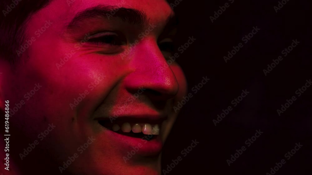 Man smiles and laughs in a dark room lit up by a screen in red Man smiles and laughs in a dark room lit up by a screen in red