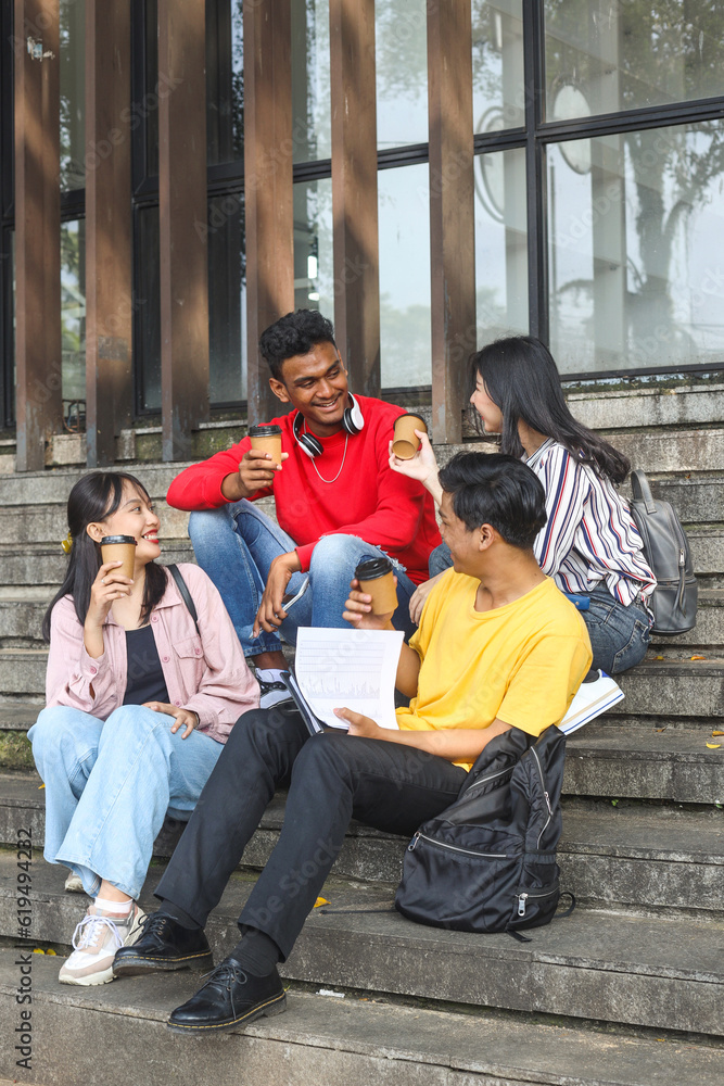 Fototapeta premium Diverse millennial young college students smiling enjoying pleasant conversation in campus staircase while drinking coffee