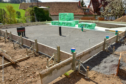 Frisch gegossene Bodenplatte eines Einfamilienhaus-Neubaus mit einbetonierten Ver- und Entsorgungsanschlüssen in der Schalung