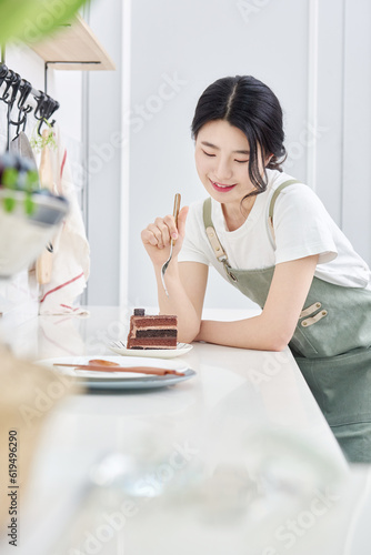young Asian female model who makes a piece of cake in the kitchen and eats it deliciously