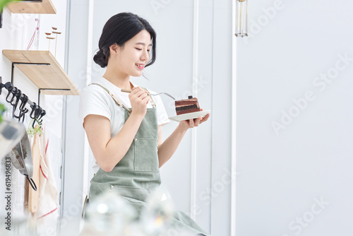 young Asian female model who makes a piece of cake in the kitchen and eats it deliciously
