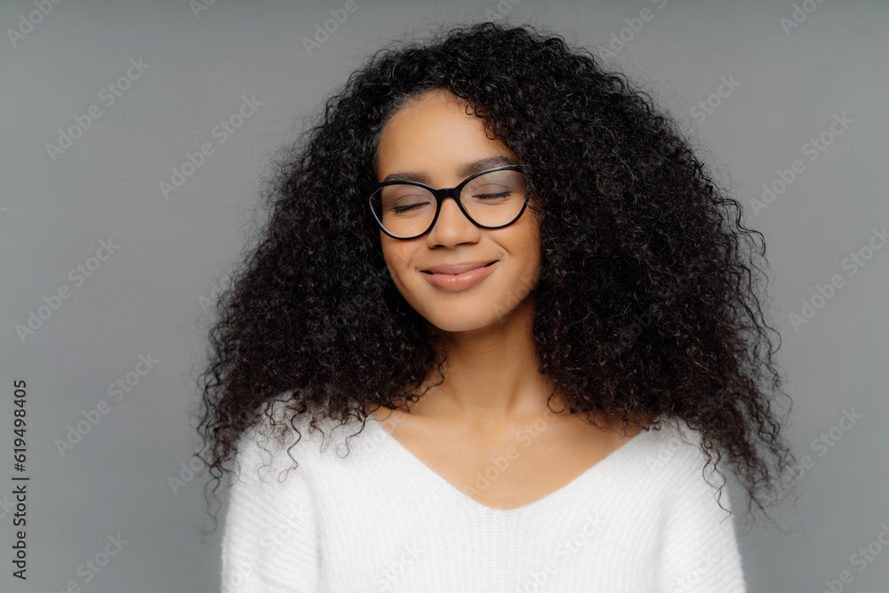 Smiling woman, bushy hair, closed eyes, glasses, white jumper, imagines, dark grey wall Smiling woman, bushy hair, closed eyes, glasses, white jumper, imagines, dark grey wall