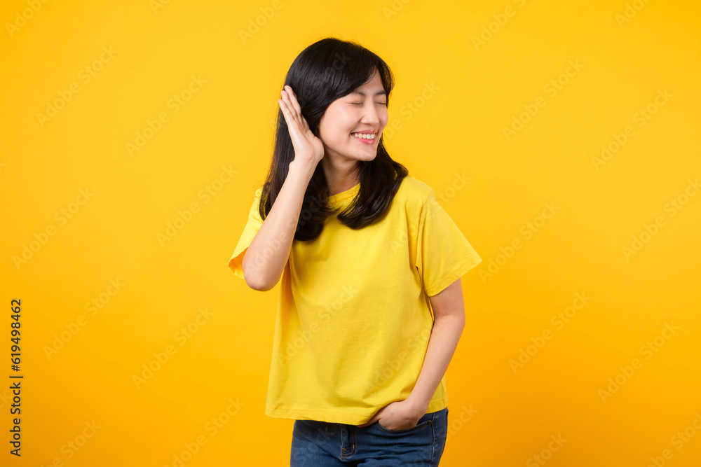 Capture attention portrait of young Asian woman. Wearing a yellow t-shirt and denim jeans, leans in to overhear and listen, evoking curiosity and intrigue. attention-grabbing promotions and discounts. Capture attention portrait of young Asian woman. Wearing a yellow t-shirt and denim jeans, leans in to overhear and listen, evoking curiosity and intrigue. attention-grabbing promotions and discounts.