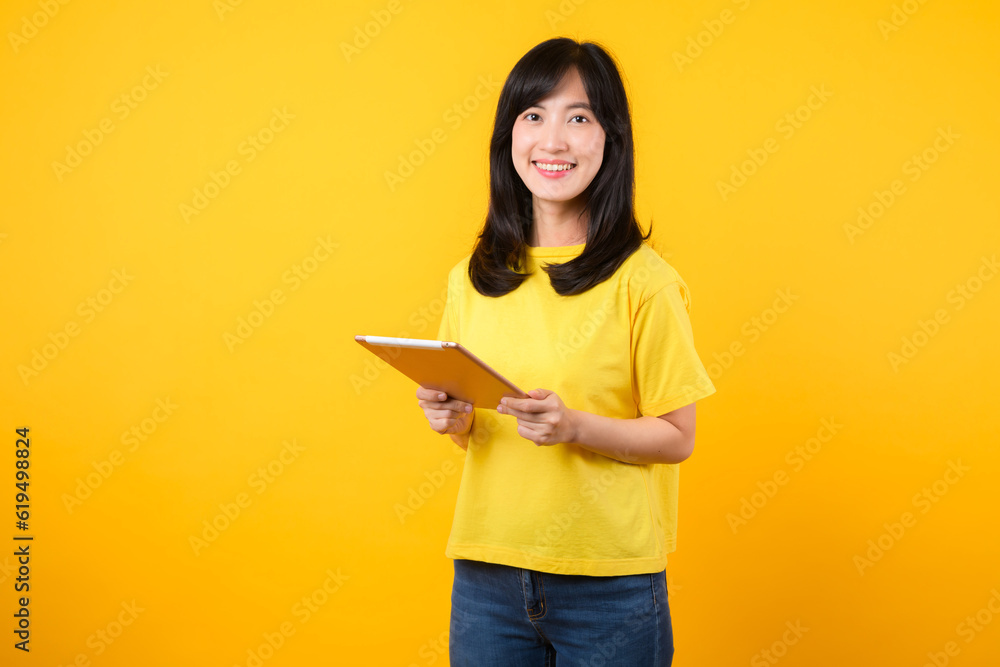 Experience the joy of education technology with portrait. A young Asian woman wearing a yellow t-shirt and denim jeans showcases a happy smile while using digital tablet. education technology concept. Experience the joy of education technology with portrait. A young Asian woman wearing a yellow t-shirt and denim jeans showcases a happy smile while using digital tablet. education technology concept.