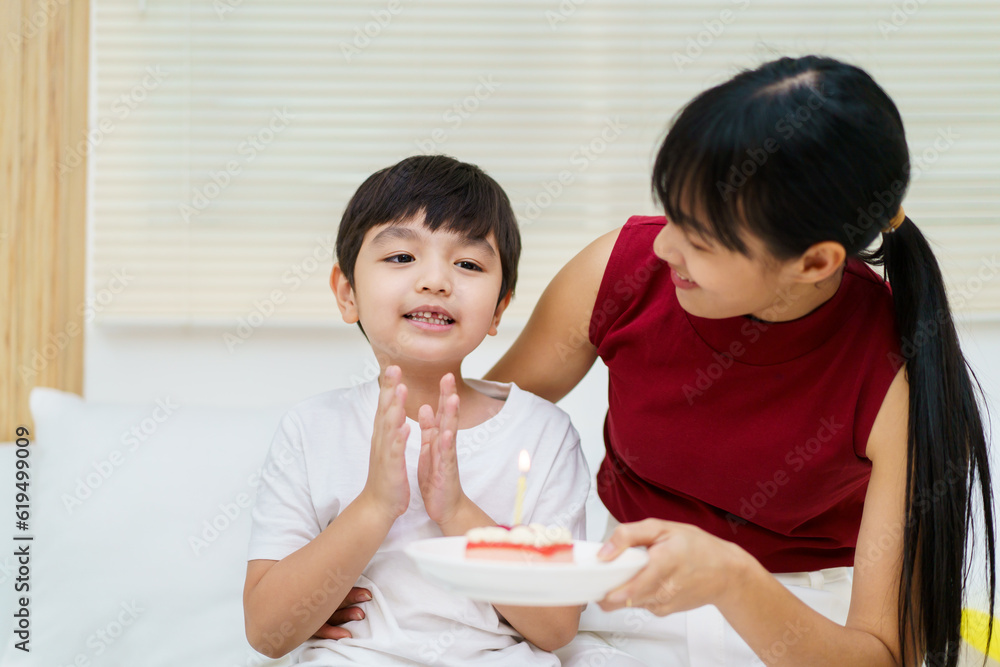 Happy cheerful Asian woman celebrating a birthday with a birthday cake for little young boy and the boy praying before blowing a candle. Happy cheerful Asian woman celebrating a birthday with a birthday cake for little young boy and the boy praying before blowing a candle.