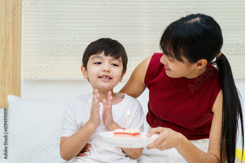 Happy cheerful Asian woman celebrating a birthday with a birthday cake for little young boy and the boy praying before blowing a candle.