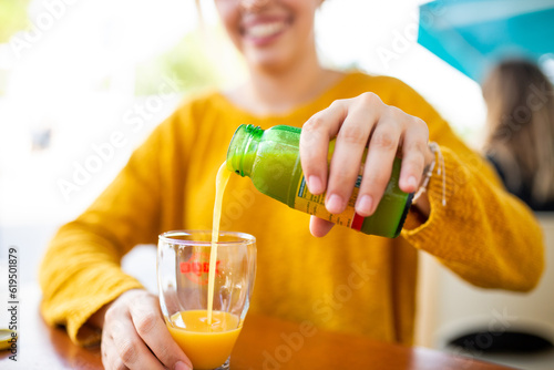 Woman pouring orange juice in glass from bottle sitting at cafe