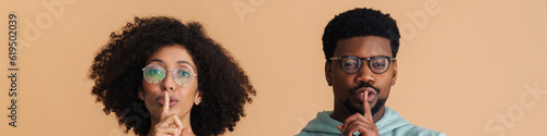 Black man and woman wearing eyeglasses doing silence gesture