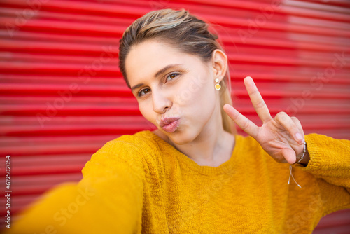 Fotografi Pretty young woman with pout and peace hand sign taking selfie