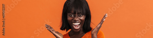 Surprised pretty african woman throwing up hands on orange background