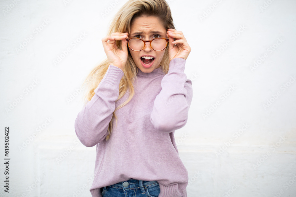 Young woman with glasses looking surprised against white wall Young woman with glasses looking surprised against white wall