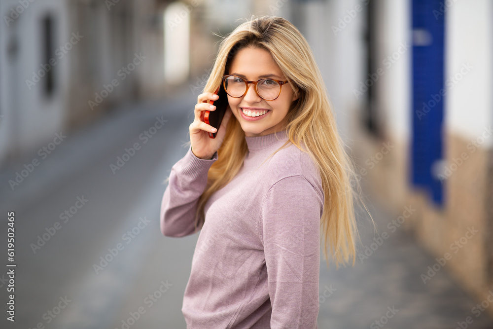 Obraz premium Attractive young woman looking behind and talking on mobile phone in city