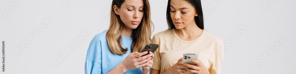 Two young brunette women posing at camera with cellphones Two young brunette women posing at camera with cellphones