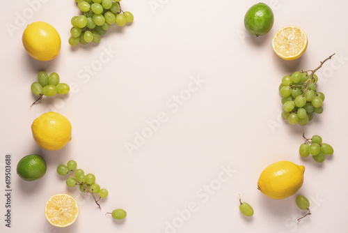 Fruits in yellow and green colors on light table with copy space. Lemon, lime and grapes frame food background