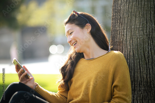 Beautiful asian woman sitting by a tree text messaging on mobile phone outside
