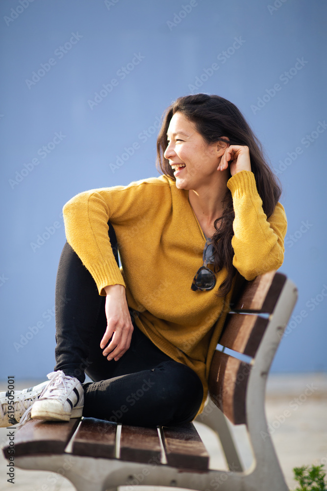Φωτογραφία Cheerful young asian woman sitting on bench outside