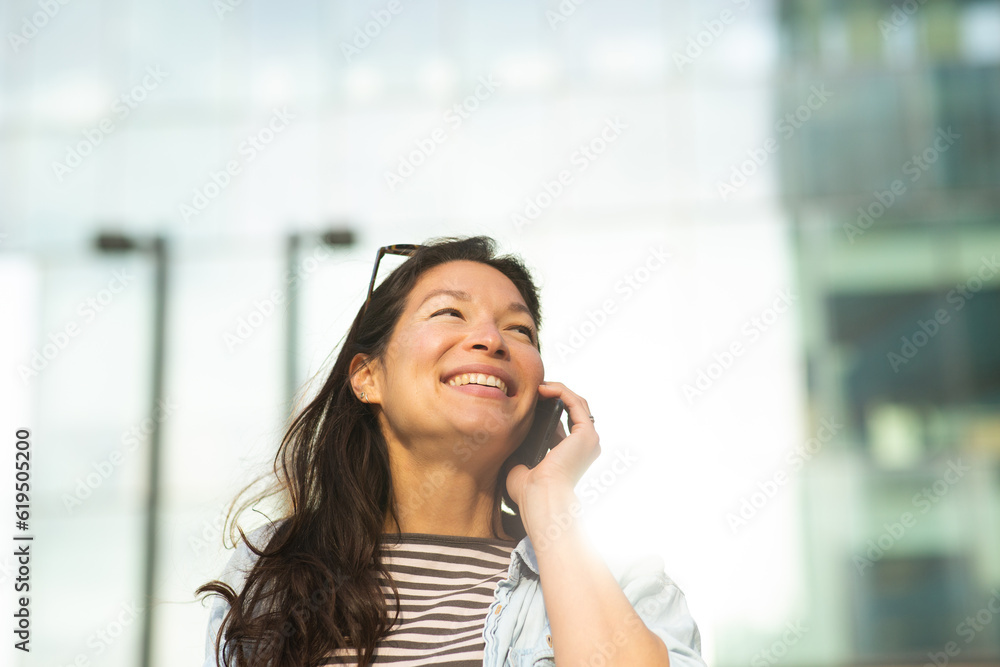 Cheerful asian woman talking on cell phone walking in the city Cheerful asian woman talking on cell phone walking in the city