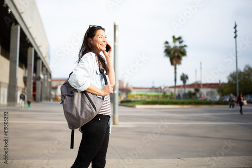 Happy young asian woman talking on mobile phone outside in city © mimagephotos