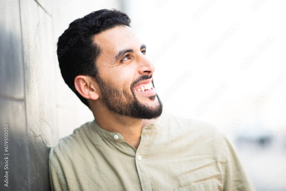 Obraz premium Smiling young arabic guy man leaning to a wall and looking away