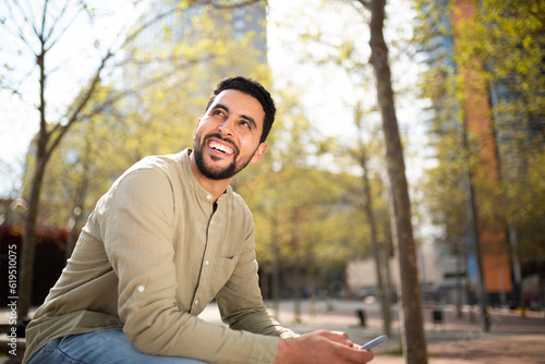Smiling young arabic man sitting outside with mobile phone