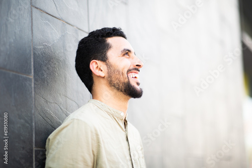 Cheerful young arab man leaning to a wall and smiling