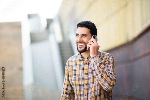 Handsome young arabic man walking outside and talking on mobile phone