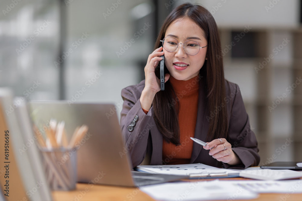Cheerful business Asian woman freelancer wear glasses making telephone call share good news about project working in office workplace, business finance concept. Cheerful business Asian woman freelancer wear glasses making telephone call share good news about project working in office workplace, business finance concept.