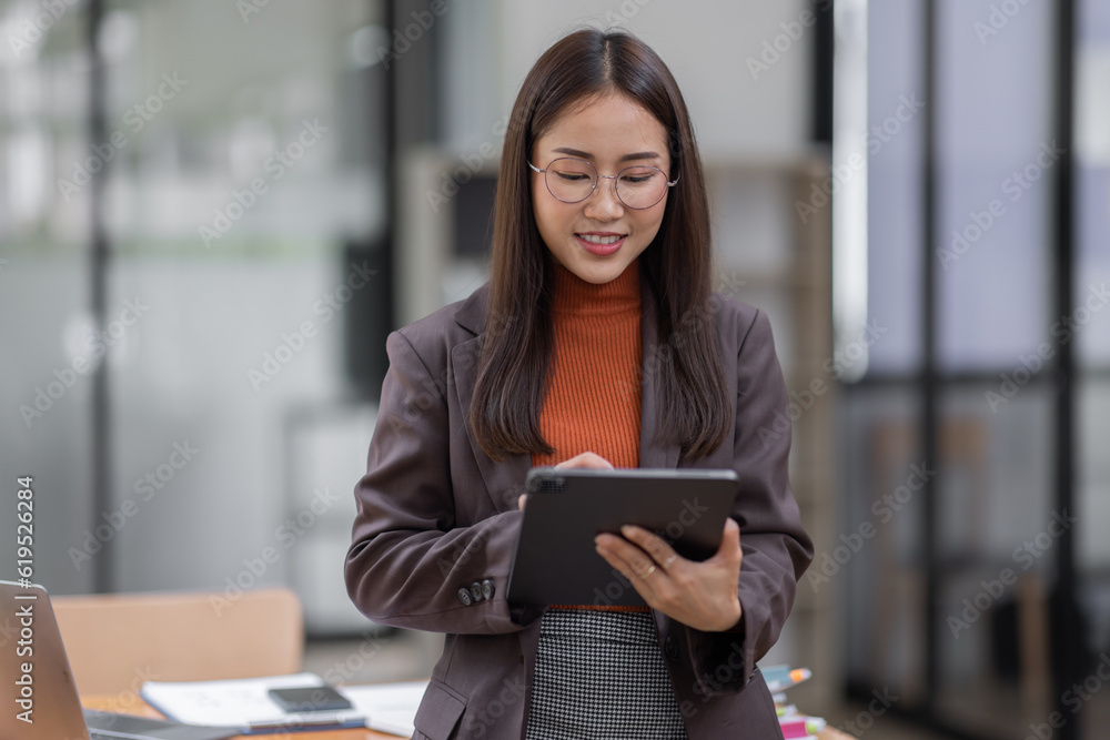 Fototapeta premium Young business entrepreneur Asian woman wear glasses using tablet , standing near the window in workplace business finance concept.