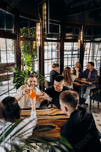 Happy group of friends drinking and clinking with beer and cocktails at brewery bar restaurant. Beverage life style concept with guys and girls having fun together