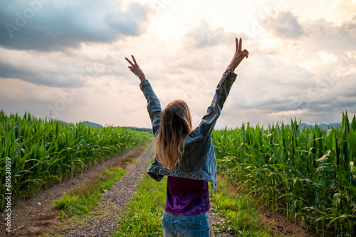 Young woman standing in the middle of green summer corn field with her arms raised high in victorious gesture photo