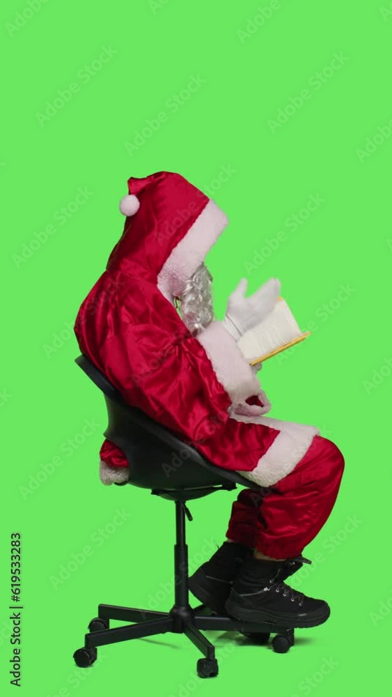 Vertical video Profile of wise santa with lecture hobby on chair reading novel story or literature, holding fiction book and sitting over full body greenscreen backdrop. Saint nick enjoying read for Vertical video Profile of wise santa with lecture hobby on chair reading novel story or literature, holding fiction book and sitting over full body greenscreen backdrop. Saint nick enjoying read for