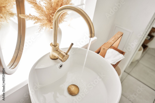 A beautiful sink with a golden faucet next to an oval mirror and a shelf with hand towels. Close-up of an elegant golden faucet in the bathroom sink next to stylish decorations.