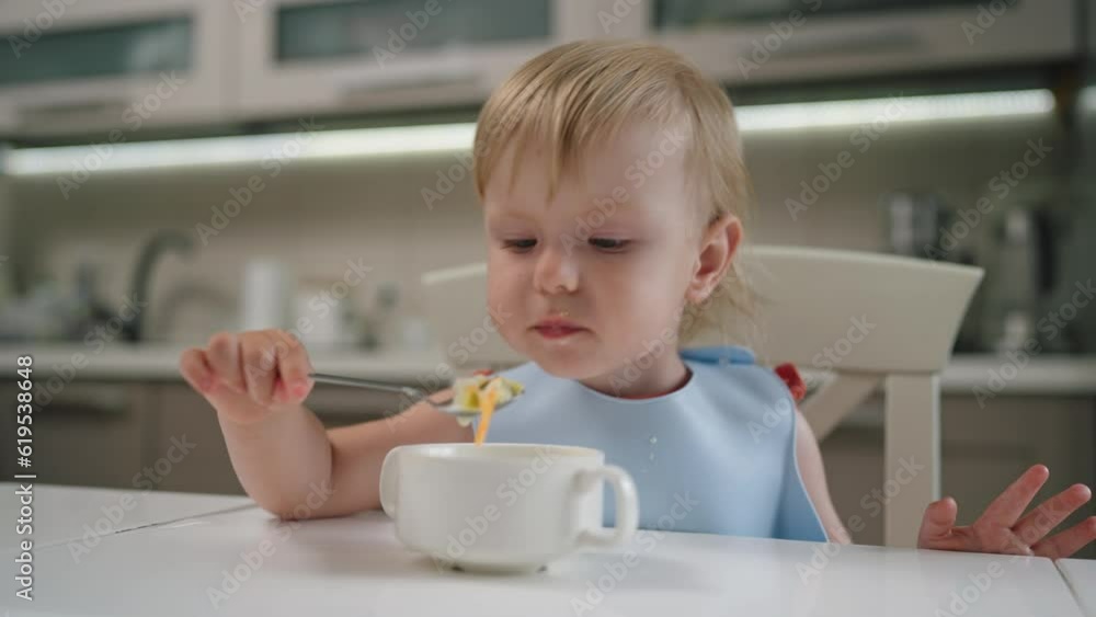 Little girl with blond hair sitting at dining table in kitchen eating homemade food with a spoon. Healthy eating and growth of kid. 2 year old toddler baby infant. Little girl with blond hair sitting at dining table in kitchen eating homemade food with a spoon. Healthy eating and growth of kid. 2 year old toddler baby infant.