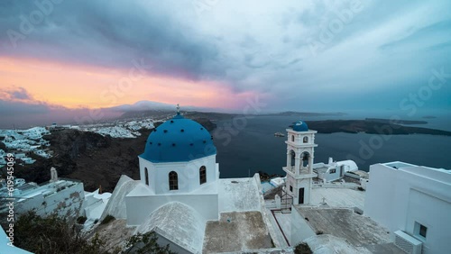 Time lapse of sunrise with colouring clouds with view on white and blue church and the caldera cliff on the Greek island of Santorini photo