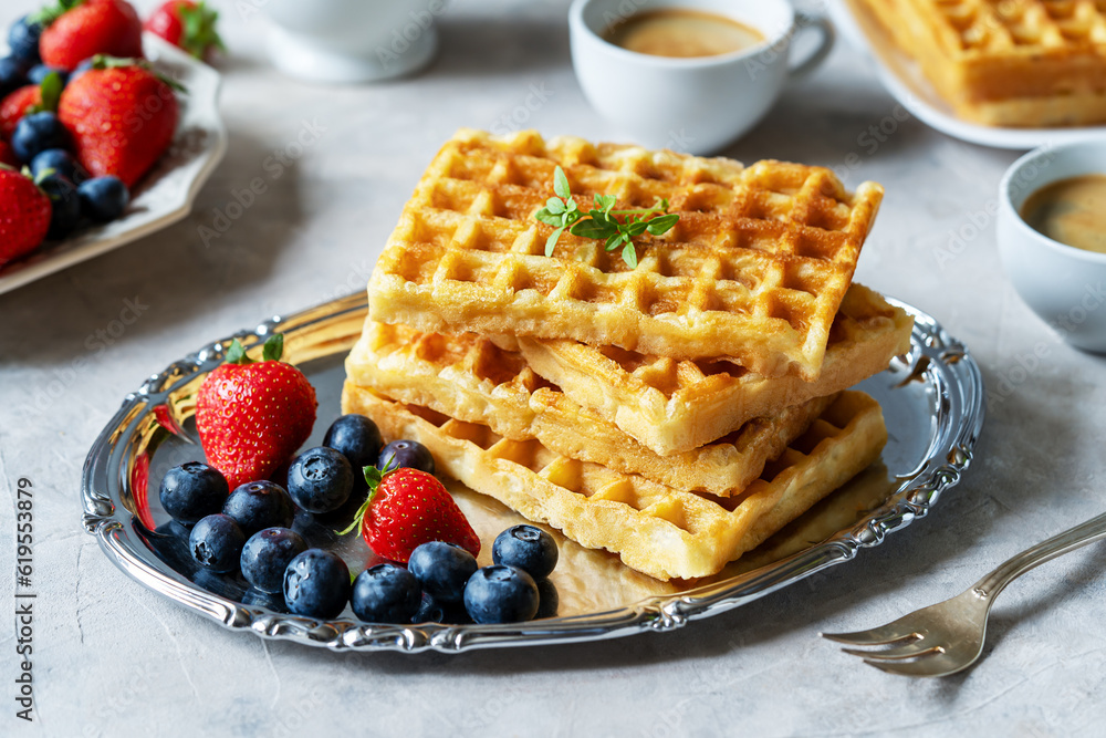 Belgian waffles with berries on silver plate, blueberries, strawberries, two cups of coffee on concrete background Belgian waffles with berries on silver plate, blueberries, strawberries, two cups of coffee on concrete background