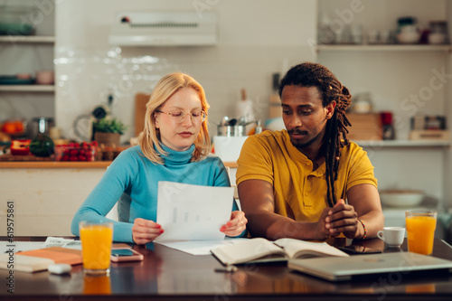 A serious interracial couple is sitting at home and looking at bills and taxes.