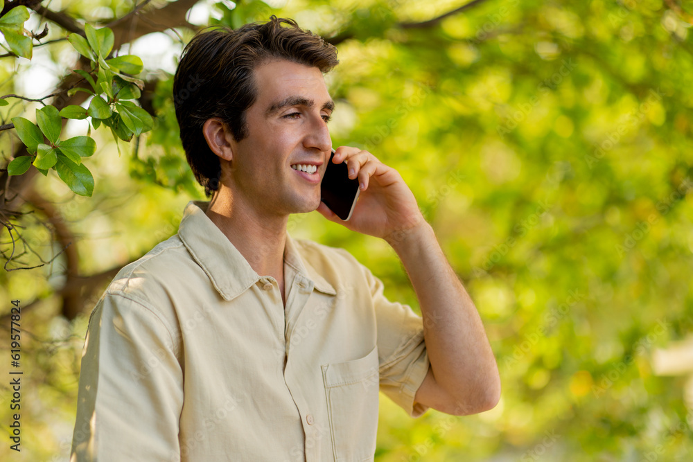 Closeup of handsome young man talking on phone at park Closeup of handsome young man talking on phone at park