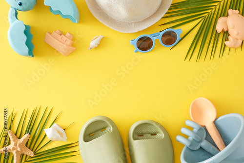 Idea of children's summer vacation on the beach. Top view flat lay of sandbox toys, eyeglasses, palm leaves, beach footwear, sun hat, seashells on yellow background with space for promo or text