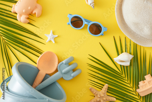 Concept of children's summer holiday. Top view flat lay of sandbox toys, eyeglasses, palm leaves, panama hat, seashells, starfish on yellow background