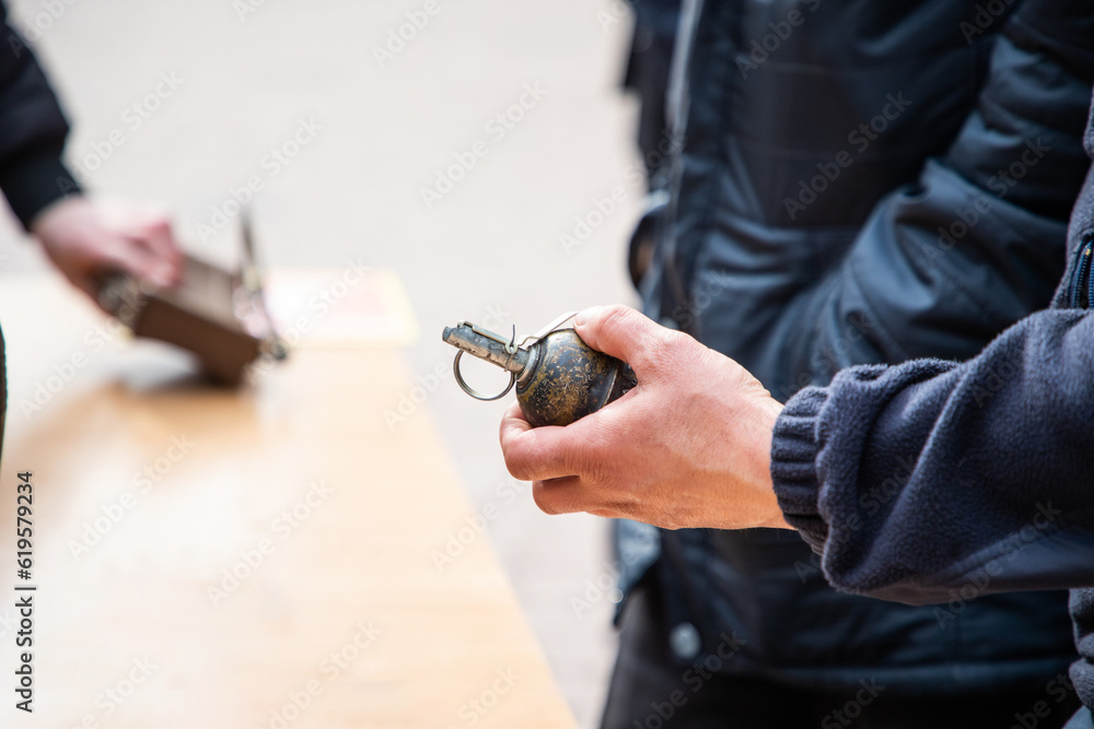 Fototapeta premium A man holds a military grenade in his hand. Military weapons, mines and grenades russian production. Military training. Demonstration military projectiles. Armed conflict. War in Ukraine. 