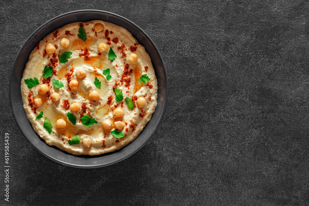 Hummus with oil and ground red pepper, chickpeas, green parsley on dark background, top view, space to copy text Hummus with oil and ground red pepper, chickpeas, green parsley on dark background, top view, space to copy text