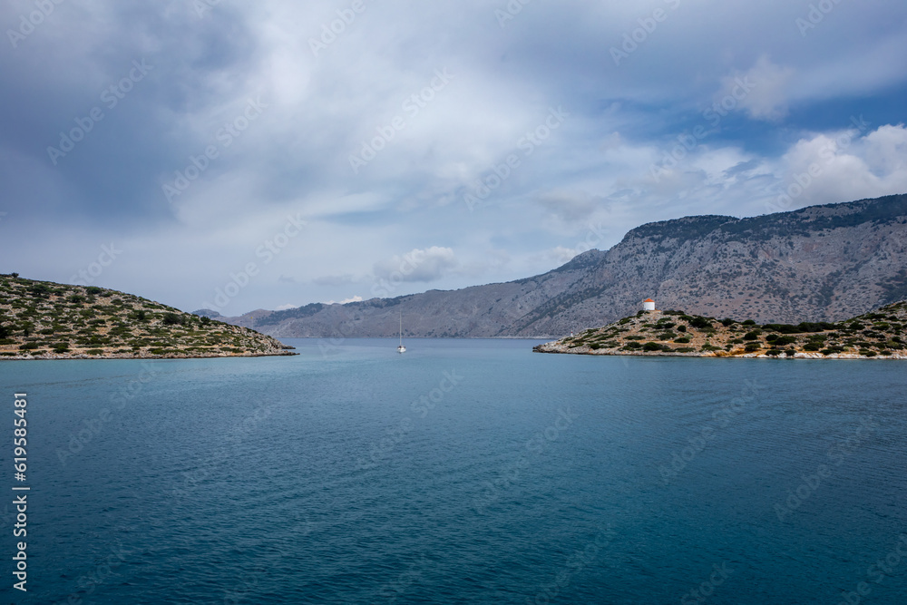 Landscape of Panormitis bay, Symi island, Greece. Blue sea water, white windmill on the hill. 
