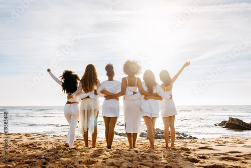 Bride\'s team. Back view of group of young diverse women posing and embracing by the seashore. Hen party celebration