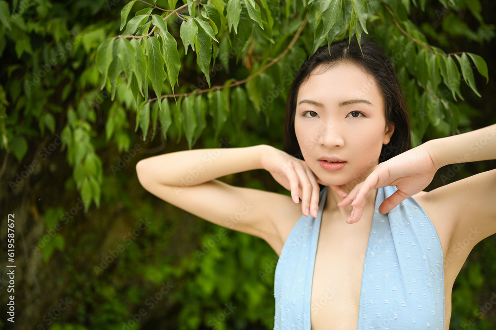 Close up outdoor portrait of Beautiful young happy Chinese Asian woman perfect skin posing outside sunny summer day green foliage. Natural facial treatment. Cosmetology, skin care and spa. Close up outdoor portrait of Beautiful young happy Chinese Asian woman perfect skin posing outside sunny summer day green foliage. Natural facial treatment. Cosmetology, skin care and spa.