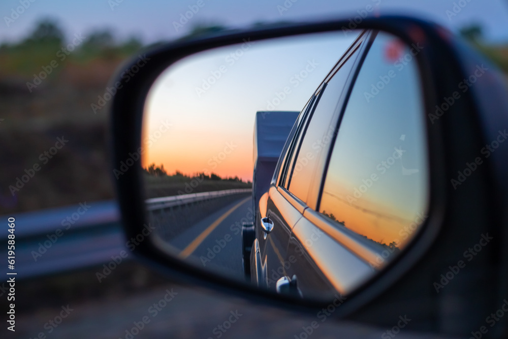 View in the side mirror of a moving car on a caravan and a sunset in the sky