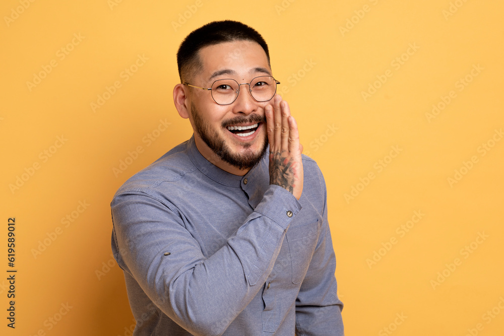 Asian Man Holding Hand Near Mouth, Sharing News Or Gossips At Camera Asian Man Holding Hand Near Mouth, Sharing News Or Gossips At Camera