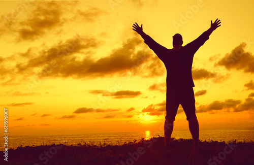 Silhouette of a man with raised-up arms at the sunset. Silhouette male raised hand in the air with success goal on sunset background. Man standing on top of coast. freedom life concept. hands up.